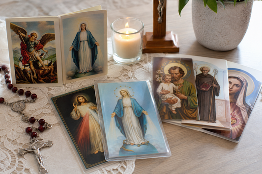 Catholic prayer cards, a rosary, and a candle arranged on a table