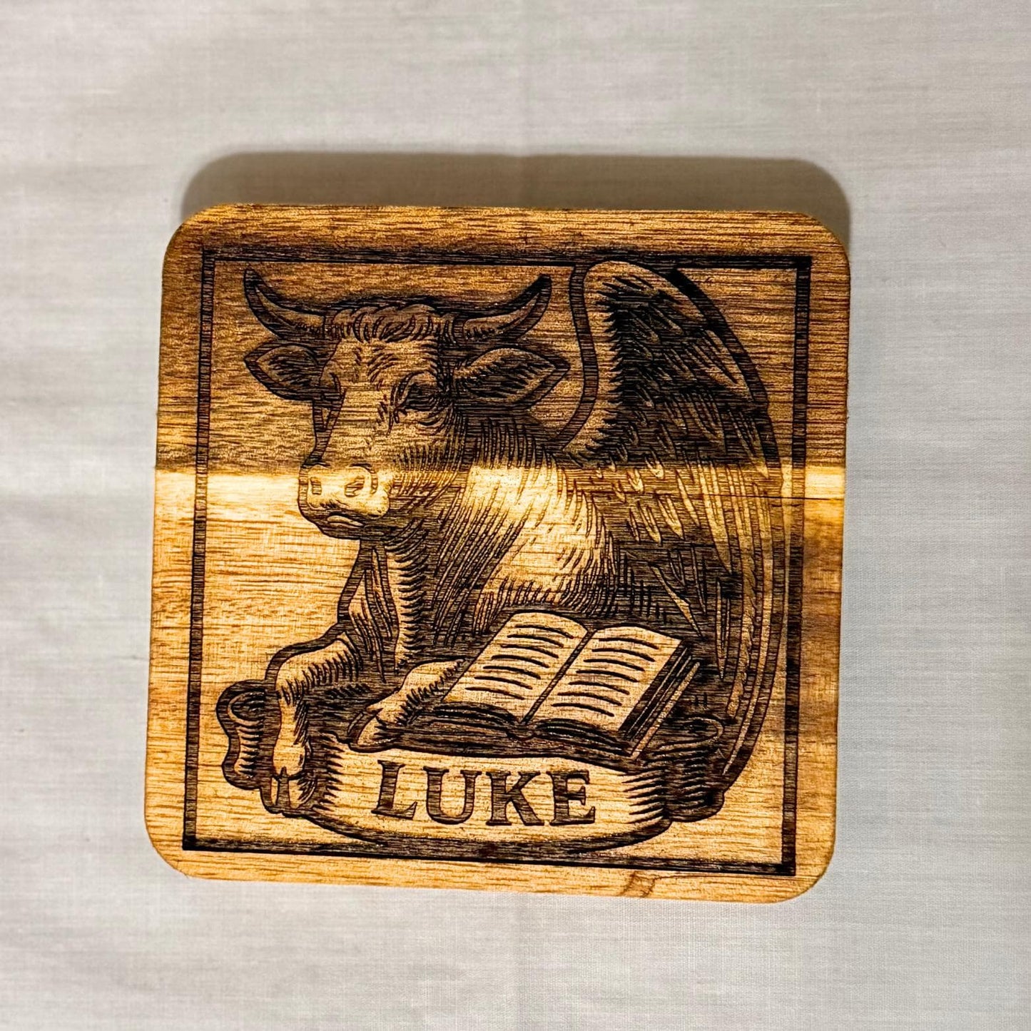 Wooden evangelist coaster set with religious Christian designs from St. Augustine Prints, featuring engraved images on natural wood.