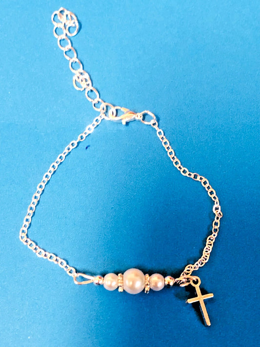 Children's glass pearl bracelet with cross charm, adjustable 7-inch length, featuring elegant pearls and a delicate cross pendant.
