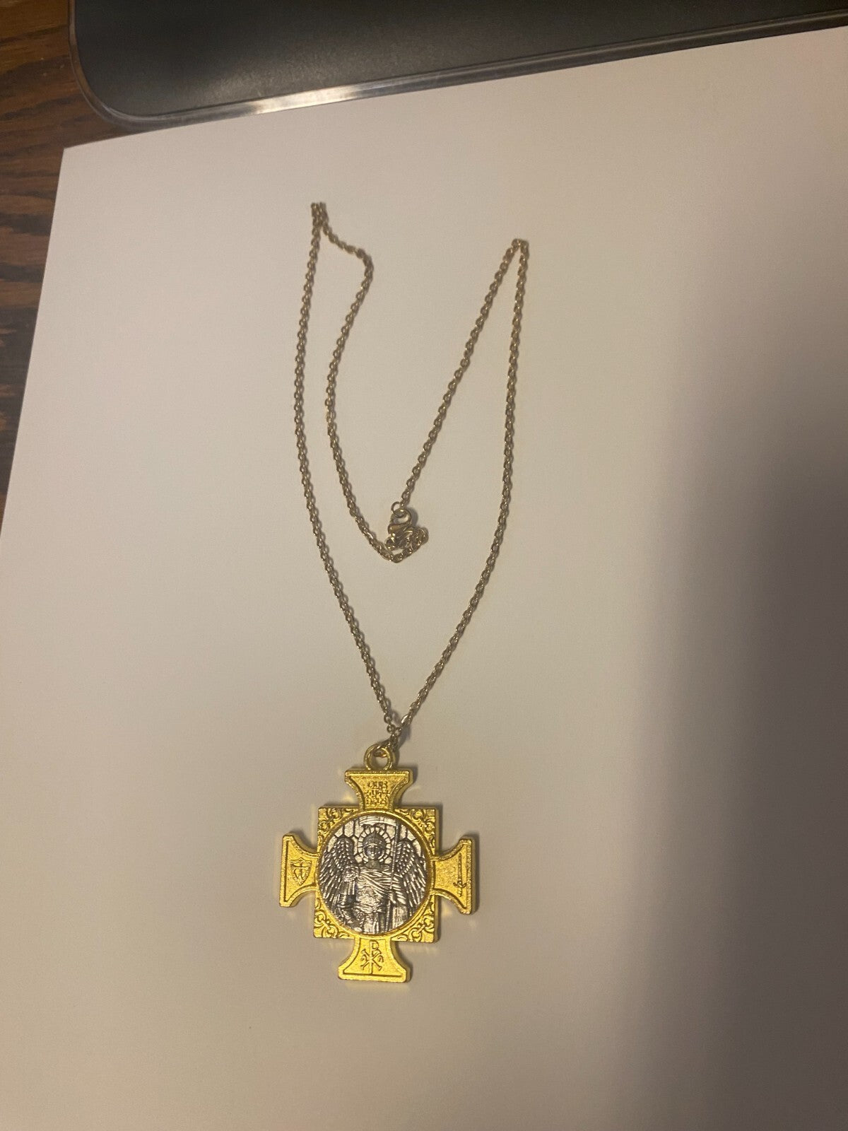 Gold and silver tone Saint Michael the Archangel iron cross pendant with detailed religious artwork on a chain.
